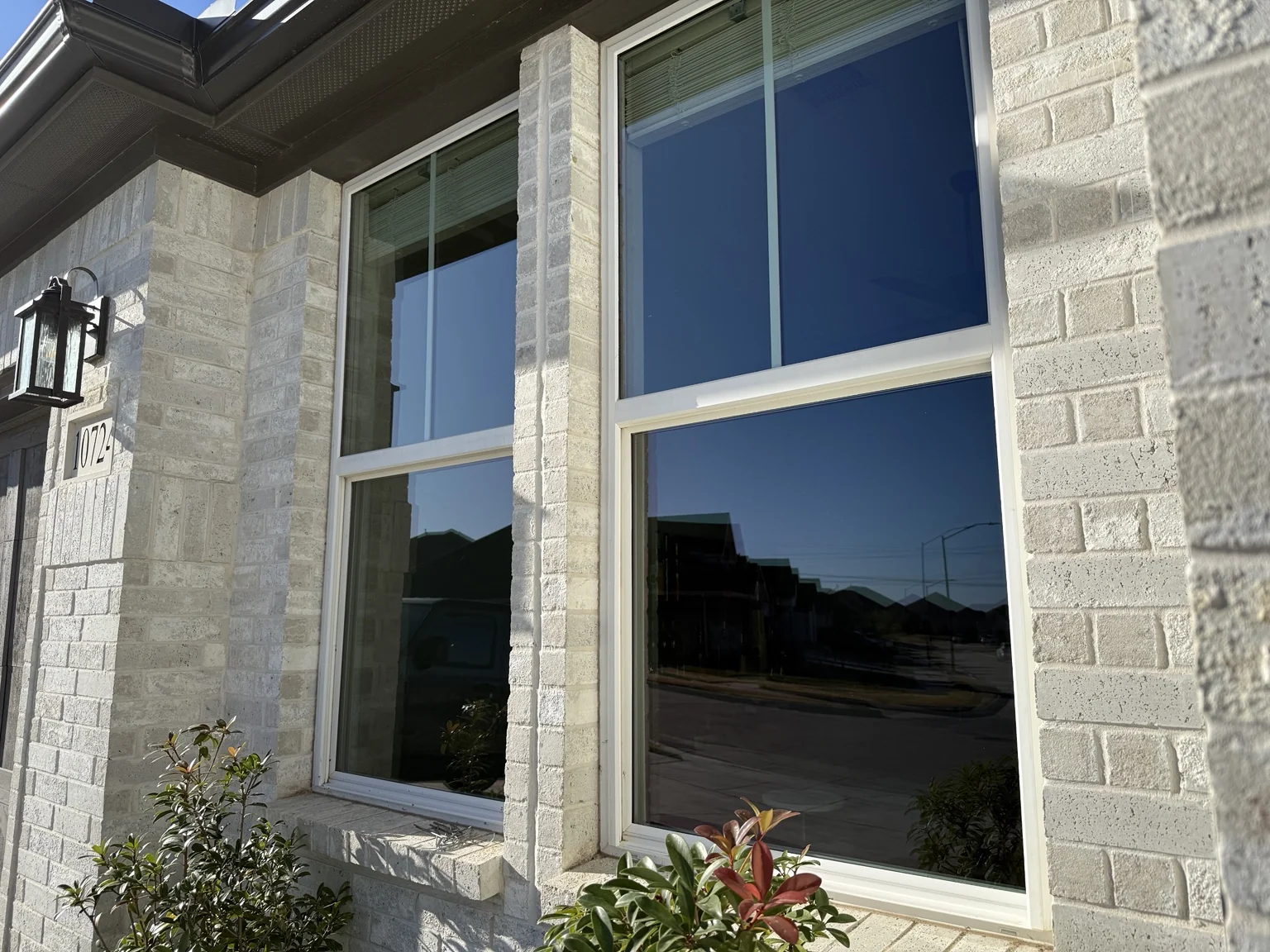 Clean front windows reflecting a blue sky on a white-brick home